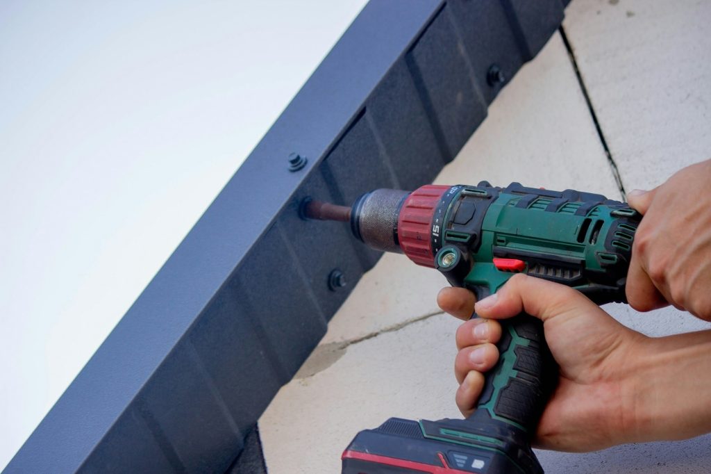 a man repairs the roof, tightens the self-tapping screw with a screwdriver
